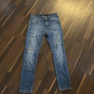 Blå slitna jeans med raka ben - Säljer ett par blå jeans med snygga slitningar på framsidan. Jeansen har klassisk femficksdesign, raka ben och slim passform. Materialet är jeans och färgen är ljusblå med tvättade detaljer. Storleken är 28/32
