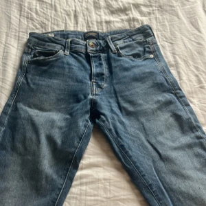 Jack and Jones blå jeans herr 28/32 slim Glenn - Säljer ett par klassiska Jack and Jones jeans. Modellen har en slim passform med raka ben och fyra fickor. Jeansen har snygga kontrastsömmar och en mörkblå tvätt som passar till allt. Perfekta för dig som gillar en tidlös och clean look.