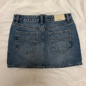 Stradivarius jeanskjol - Snygg klassisk blå jeanskjol från Stradivarius i storlek 36. Modellen är kort med fem fickor, bälteshällor och knapp framtill. Perfekt basic-plagg med cool denimlook och kontrastsömmar. Passar till allt och är superenkel att styla.