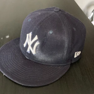 Mörkblå New Era Yankees keps 59FIFTY (St. 57,7cm) - Säljer en klassisk mörkblå New York Yankees keps från New Era, modell 59FIFTY. Kepsen har broderad Yankees-logga framtill och New Era-logga på sidan. Tillverkad i 100% polyester med rak skärm och stängd baksida. Perfekt för dig som gillar sportig streetstyle. (St. 57,7cm)