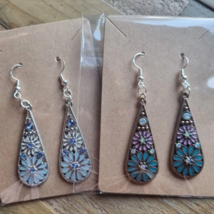 Vintage droppformade örhängen - Två par vackra örhängen med blommönster. Finns i två olika färgställningar. Örhängenskrokar gjorde av koppar. Längd 6,5 cm. Lätt vikt