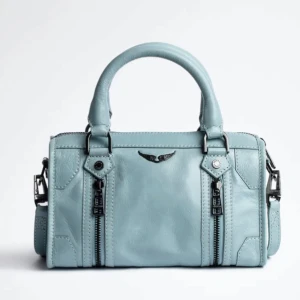 Ljusblå handväska från Zadig & Voltaire - Snygg ljusblå handväska i skinn från Zadig & Voltaire med coola svarta metalldetaljer, dubbla handtag och dragkedjor framtill. Väskan har broderad logga på axelremmen och ikoniska vingar i metall på framsidan. Perfekt för dig som vill sticka ut med en trendig accessoar. Jag kan skicka fler bilder på väskan. Ursprungligen är den köpt för nästan 5000 men säljer den för 3800