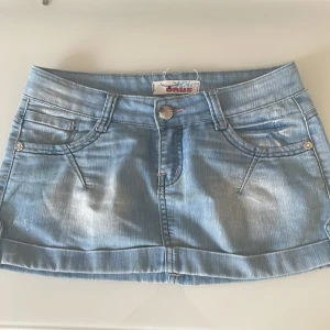 Ljusblå jeanskjol från Urus - Säljer en snygg ljusblå lågmidjade jeanskjol från Urus med klassisk femficksdesign och broderade bakfickor. Kjolen har bälteshällor, knapp och dragkedja framtill. Perfekt för dig som gillar en avslappnad och trendig stil. Midjan tvärs över är 38cm! 