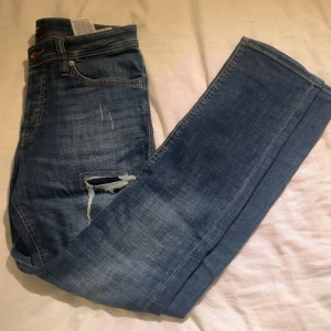 Blå slitna jeans Jack & Jones - Snygga blå jeans från Jack & Jones med slitningar och hål på benen för en cool, avslappnad look. Klassisk femficksmodell med normal passform och raka ben. Jeansen är gjorda i bomull och har detaljerade sömmar och läderpatch bak.