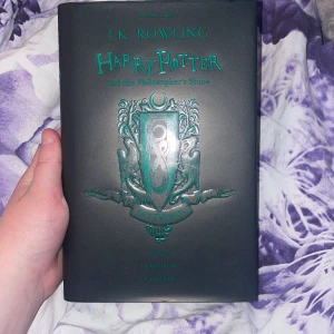 Harry Potter and the Philosopher's Stone (Slytherin Edition) - Upptäck den magiska världen med denna Slytherin-utgåva av Harry Potter! Bokens omslag och sidor har coola gröna detaljer, perfekt för dig som gillar stolthet, ambition och list. En samlarfavorit för unga fans av fantasy och äventyr.