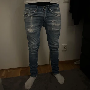 Dondup George jeans - Säljer ett par ljusblå Dondup George jeans med slitningar och trasiga detaljer framtill. Jeansen har klassisk femficksdesign. Perfekta för dig som gillar en avslappnad look.
