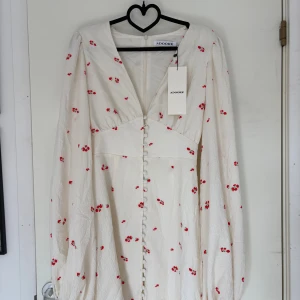 Vit blommig klänning från Adoore - Superfin vit klänning från Adoore med små röda blommor. Klänningen har v-ringad hals, långa puffärmar och knappar framtill. Materialet är lätt och krispigt, perfekt för sommarens alla tillfällen. Snygg passform som markerar midjan och ger en romantisk vibe. Ny med prislapp, nypris 1495kr