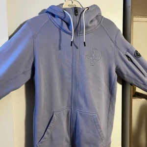 Pelle P Zip-Hoodie  - Snygg ljuslila hoodie från Pelle P med dragkedja, huva med snörning och två stora fickor fram. Broderad logga på bröstet och patch på ärmen. 
