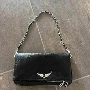 Svart axelväska med kedja och vingar - Köpte den utomlands men aldrig använd.                    ( f e j k ) den har en till kedja som jag tagit av som kommer med