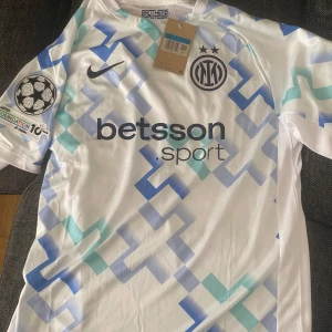 Inter Milan Bastoni Champions League tröja - Inter Milan Bastoni 95 Champions League-tröja. Vit bas med blå och turkosa geometriska mönster, kortärmad och tillverkad i lätt funktionsmaterial. UEFA Foundation-märke på ärmen och klubbmärke på bröstet. Perfekt för dig som älskar fotboll och vill sticka ut. Knappt använd 