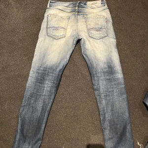 Replay Anbass ljusblå jeans - Säljer ett par Replay Anbass jeans i ljusblå tvätt med snygga slitningar och klassiska femficksdetaljer. Jeansen har smal passform och normal midja, med Replay-logga på bakfickan och dragkedjegylf. Perfekta för en avslappnad och trendig look. Storlek 30/32 men passar lite större i midjan!