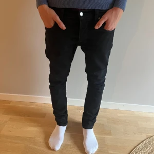  Nudie Jeans  - Säljer ett par svarta slim jeans från Nudie Jeans i storlek 30/32. De har klassisk femficksdesign, snygga svarta sömmar och Nudie Jeans logga på bakfickan. Jeansen är i stretchigt bomullsmaterial och har en slim passform som sitter slim längs benen.