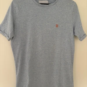 Ljusblå t-shirt Les Deux S - Ljusblå t-shirt från Les Deux med diskret melerad look och liten röd broderad II-logga på bröstet. Klassisk rund hals och korta ärmar. Mjuk och skön bomull som passar perfekt till jeans eller shorts. Enkel och stilren design från Köpenhamn.
