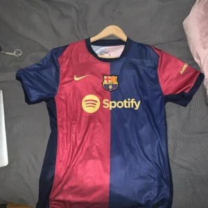 Barcelona t shirt - Säljer en snygg fotbollströja från Nike i blått och rött med klubbmärke och sponsorlogga på framsidan. Tröjan är kortärmad och tillverkad i Dri-FIT-material för optimal komfort. Perfekt för fotbollsfans som vill visa sitt stöd.
