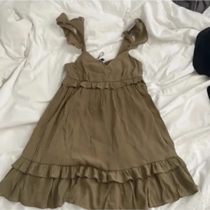 Grön klänning med volangdetaljer - Säljer en söt grön klänning från Zara med volangdetaljer och knytband på axlarna. Klänningen har en v-ringad design och är perfekt för varma dagar. Den är kort och har en luftig passform.