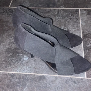 Svarta klackskor från Savita - Snygga svarta klackskor från Savita med en elegant design. Skorna har en spetsig tå och är tillverkade i ett stretchigt material som ger en bekväm passform. Perfekta för att ge en stilren touch till din outfit.