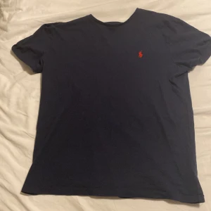 Mörkblå t-shirt från Ralph Lauren - Säljer en stilren mörkblå t-shirt från Ralph Lauren med det klassiska röda broderade logotypen på bröstet. Perfekt för en avslappnad look.