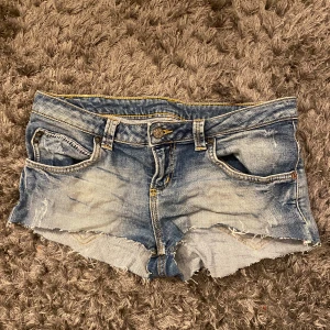 Blå jeansshorts - Säljer ett par snygga blå jeansshorts med fransiga kanter och slitna detaljer. Shortsen har en klassisk femficksdesign och knappgylf. Perfekta för en avslappnad stil. Hör av dig vid frågor❤️