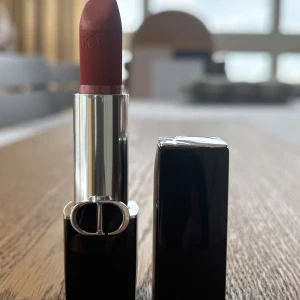 Rött läppstift från Dior - Elegant rött läppstift från Dior i nyansen 720 Icone Velvet. Läppstiftet har en lyxig svart hylsa med silverdetaljer och den ikoniska CD-loggan. Perfekt för att ge en sofistikerad touch till din look.