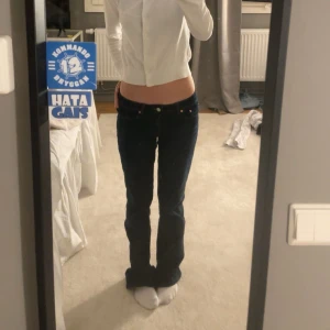 Mörkblå bootcut jeans - Snygga mörkblå bootcut jeans med låg midja och klassisk femficksdesign. Jeansen har en stilren look med subtila sömmar och knappar i silverfärg. 