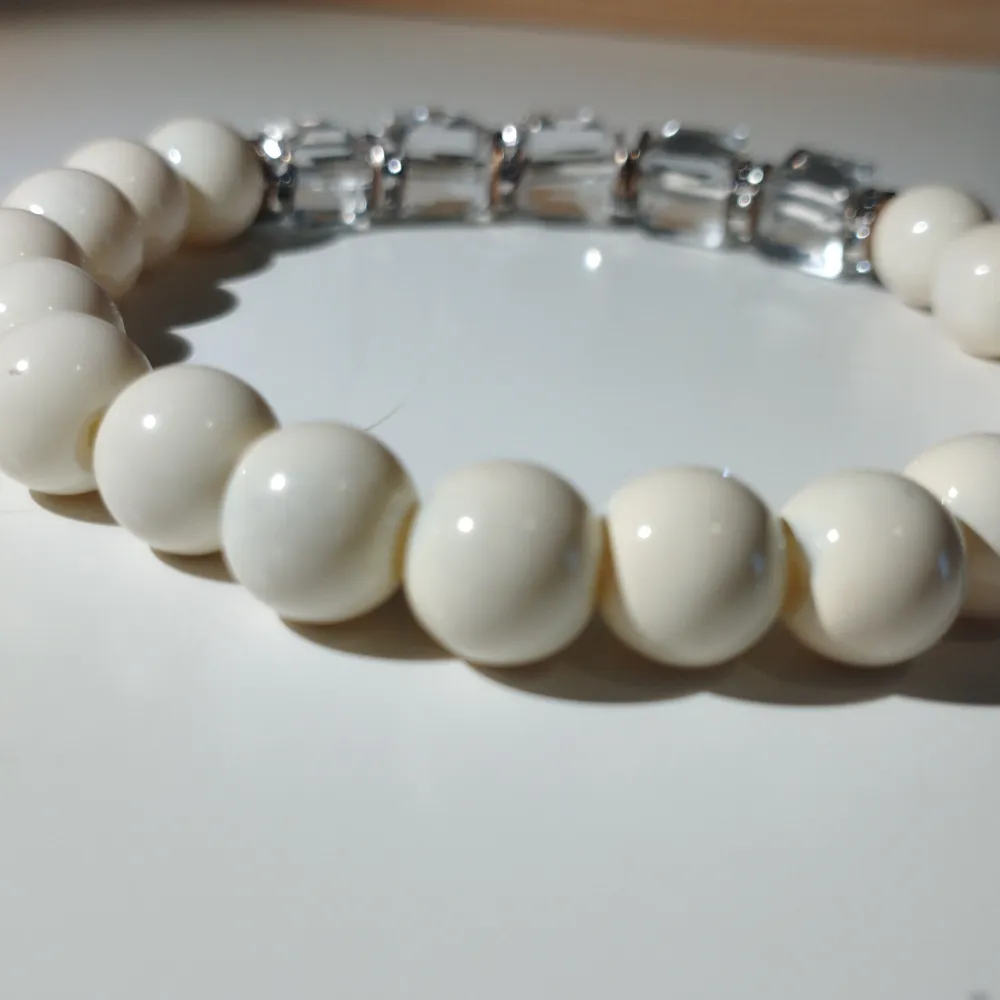 Elegant armband med vita runda pärlor och klara, facetterade pärlor som ger en glittrig effekt. Perfekt för att lägga till en touch av stil till din outfit. Armbandet är 6 cm i diameter och cirka 16 cm i omkrets.. Asusteet.