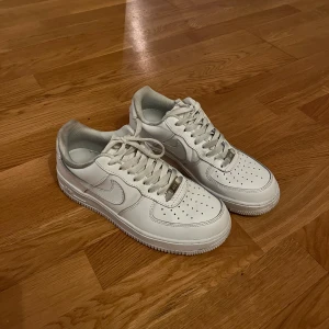 Vita Nike Air Force sneakers - Säljer ett par klassiska vita Nike Air Force sneakers. De har en stilren design med snörning och perforerade detaljer på ovansidan för ventilation. Perfekta för en casual look. Använda 2 gånger.