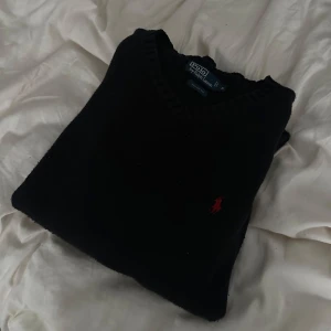 Svart tröja från Polo Ralph Lauren - Säljer en stilren svart tröja från Polo Ralph Lauren i 100% bomull. Tröjan har en diskret röd logga på bröstet och en klassisk v-ringad design. Perfekt för en avslappnad men ändå elegant look. Passar S/M (själv storlek M) och passar mig fint  ! Säljs billigt då det finns ett hål vid baksidan som är jätte litet, syns inte när man har på sig, går att sy upp! !