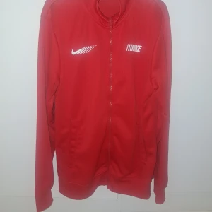 röd kofta från Nike - Säljer en röd kofta från Nike med dragkedja framtill. Jackan har långa ärmar och två fickor. Perfekt för sportiga aktiviteter eller som en snygg vardagskofta. Nike-loggan syns tydligt på bröstet.