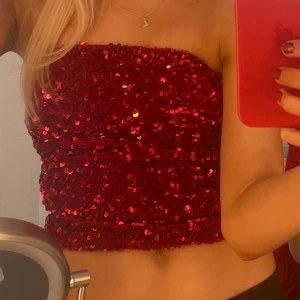 Röd paljett topp  - Säljer en glittrig röd tubtopp täckt med paljetter. Perfekt för att sticka ut på festen! Toppen är ärmlös och har en tight passform.