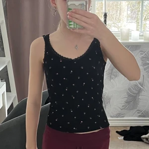 Svart blommig linne med spetsdetaljer - Säljer ett sött svart linne med små rosa blommor och gröna blad. Toppen har spetsdetaljer vid halsringningen och axelbanden samt en liten rosett framtill. Perfekt för en somrig look! Har sytt upp banden lite men det går och ta bort om man vill. Använd 4 gånger. Kostade 100 kr när jag köpte den. Super söt och jätte skön! 😍