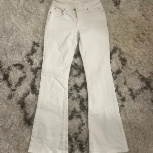 Vita lågmidjade bootcut jeans - Snygga vita bootcut jeans med låg midja. De har en klassisk femficksdesign och stängs med dragkedja och knapp. Perfekta för en stilren look.