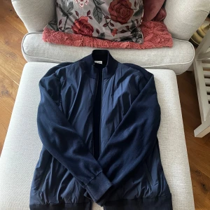 Mörkblå Cardigan från John Henric - Säljer en stilren mörkblå cardigan från John Henric. Cardigenen har en klassisk design med ribbade muddar och krage. Perfekt för en snygg och avslappnad look.