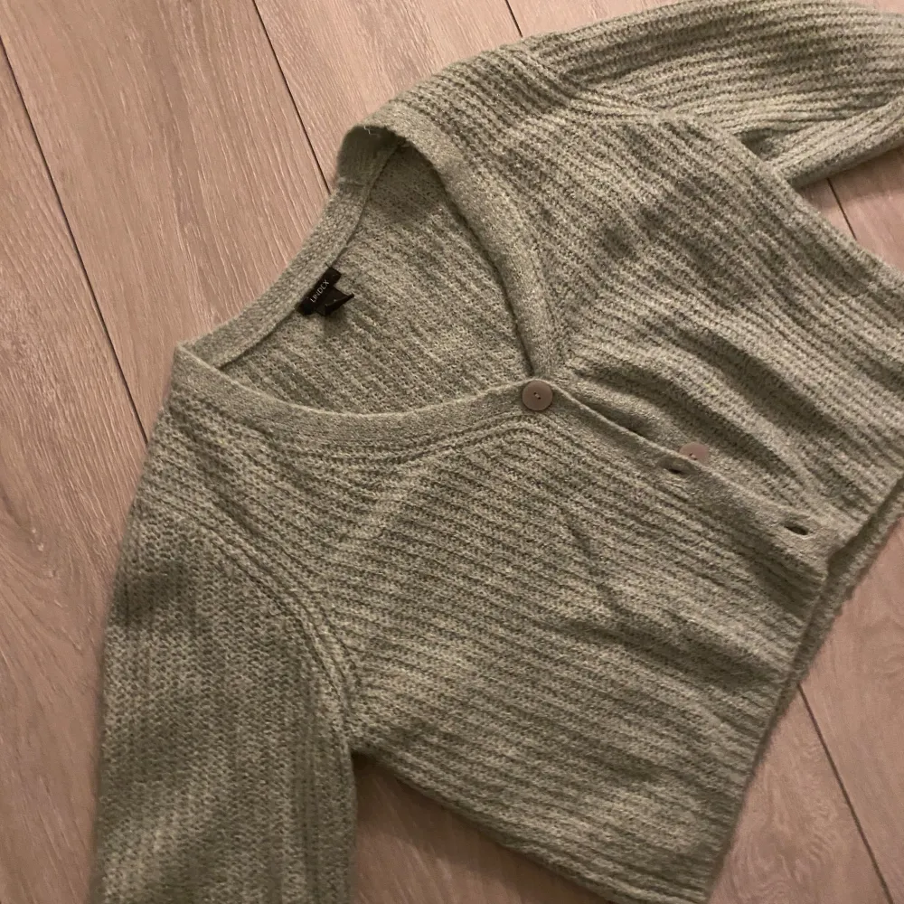 Mysig grön stickad kofta från Lindex med knappar framtill. trekvartärm, Perfekt för kyliga dagar och ger en avslappnad look. Koftan har en mjuk textur och en klassisk design.. Neuletakit & Villapaidat.