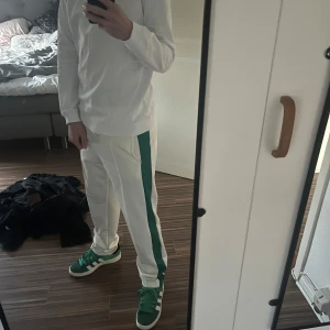 Vita mjukisbyxor med grön rand - Snygga vita mjukisbyxor med en grön rand längs sidorna. Perfekta för en avslappnad stil och bekväma att bära. Passar bra till sneakers och en enkel tröja.