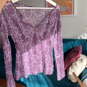 Mönstrad lila topp - Säljer en snygg lila topp med ett detaljerat mönster. Toppen har långa ärmar som blir vidare nedtill, och en v-ringad design som ger en elegant touch. Perfekt för att piffa upp garderoben! Den är åt det genomskinliga hållet och har en snygg söm som markerar bysten mellan xs-m beror på hur man vill att den sitter