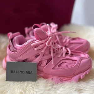 Rosa sneakers från Balenciaga - Snygga rosa sneakers från Balenciaga med en chunky sula och detaljerad design. Skorna har snörning och är perfekta för att ge en färgklick till din outfit. Balenciaga-loggan syns både på sidan och under sulan.