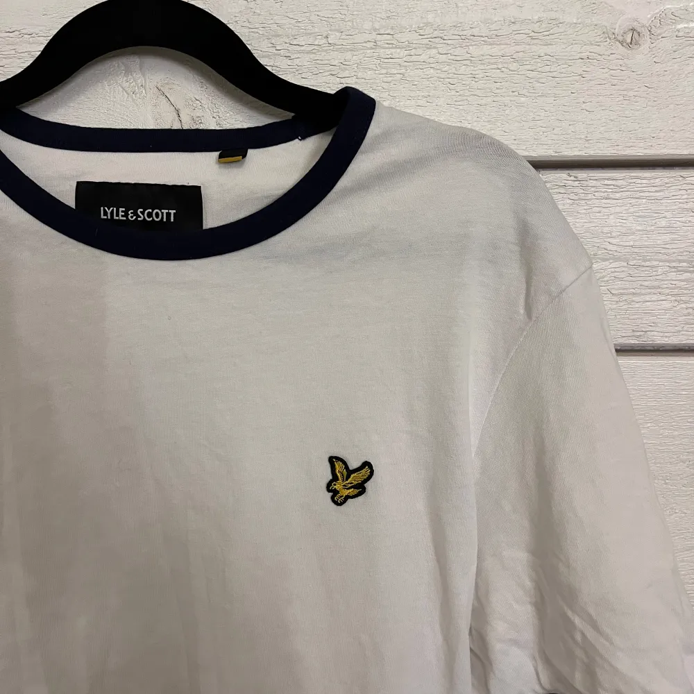 Säljer en stilren vit t-shirt från Lyle & Scott med mörkblå detaljer vid krage och ärmslut. Den har en liten broderad logga på bröstet. Perfekt nu till våren🌸. T-paidat.