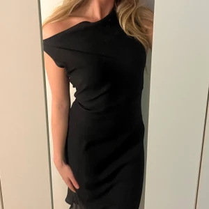 Svart one-shoulder klänning - Snygg svart klänning med one-shoulder design. Perfekt för en elegant kväll med sin stilrena look. Klänningen har en figurnära passform som framhäver silhuetten.