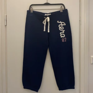 Blå mjukisbyxor från Aéropostale - Säljer ett par bekväma blå mjukisbyxor från Aéropostale med vit snörning i midjan och tryck på sidan. Byxorna är perfekta för en avslappnad stil och har en elastisk midja för extra komfort.