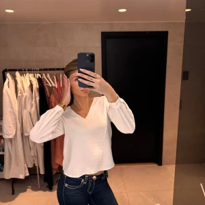 Vit blus med v-ringning - Säljer en stilren vit blus med v-ringning och långa ärmar. Perfekt för en chic och enkel look.