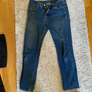 Levis 501 jeans - Klassiska Levis 501 jeans i blå denim. De har en rak passform. Perfekta för en avslappnad stil med fem fickor och knappgylf. Storlek 32/32. Liten färgfläck på vänstra benet. 