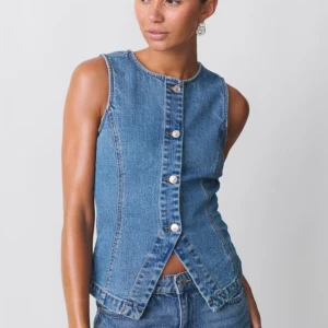 Jeansväst med knappar - Snygg jeansväst i blå denim med knappar framtill. Västen har en figurnära passform och är ärmlös, vilket ger en stilren look. Perfekt för att lägga till en cool touch till din outfit. Västen är slutsåld och endast använd en gång! Bilderna är lånade från Gina tricot men bild nummer två är min. 