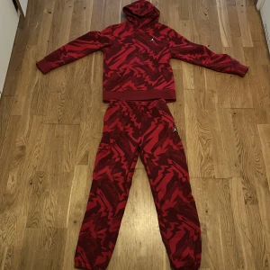 Röd hoodie och byxor från Jordan - Säljer en cool röd hoodie och matchande byxor från Jordan med ett unikt mönster. Hoodien har långa ärmar och en klassisk huva. (TRÖJAN OCH BYXORNA ÄR I STORLEK M)