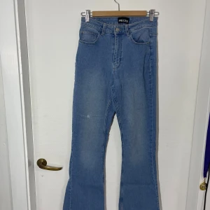 Bootcut jeans från Pieces - Snygga blå jeans från Pieces med klassisk femficksdesign och knappgylf. De har en utsvängd passform och är perfekta för en avslappnad stil. Jeansen har en ljusblå tvätt som ger en fräsch look. Uppsydda nedtill. Liten vit fläck framtill.