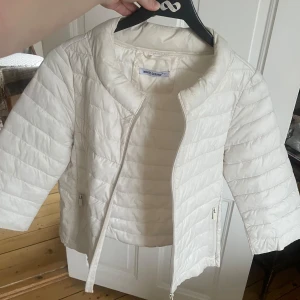 Vit quiltad jacka med trekvarts ärmar - Säljer en stilren vit quiltad jacka från Monte cervino. Jackan har en dragkedja framtill och trekvartsärmar, vilket ger en modern look. Perfekt för vår och sommar. Den är lätt och bekväm att bära.
