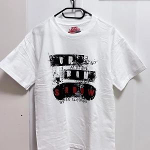 Vit t-shirt med tryck från Urban Shadow - Snygg vit t-shirt från Urban Shadow med ett coolt svart och rött tryck på framsidan. Perfekt för en avslappnad stil. Kortärmad och tillverkad i mjukt material.