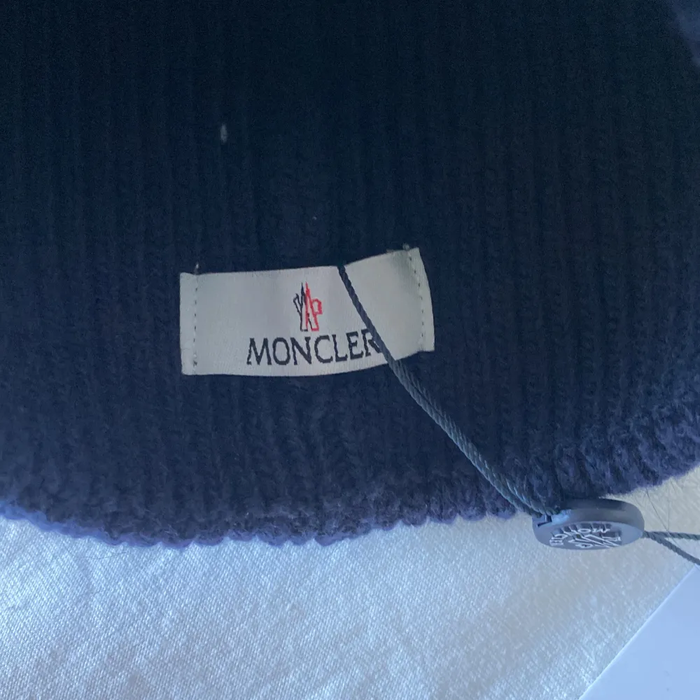 Snygg mörkblå mössa från Moncler med ribbad design och uppvikt kant. Den har en broderad Moncler-logga framtill. Perfekt för att hålla värmen med stil.. Asusteet.