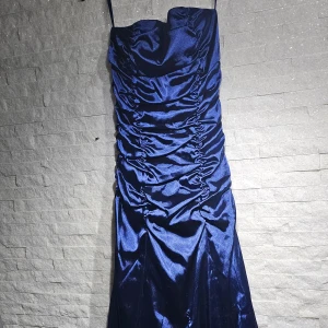 Balklänning. Marinblå sidenklänning med snörning - Snygg marinblå klänning i siden med smala axelband och en elegant snörning framtill. Klänningen har en åtsittande passform med rynkade detaljer som ger en lyxig känsla. Perfekt för en kväll ute eller en speciell tillställning. Använd en gång. Nypris 3500:- inköpt på guldgalgens, balaffär.