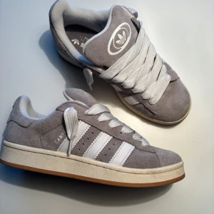 Adidas Campus 00 ”Grey White” - Adidas Campus 00s med färgen ”Grey White”. Använda ett fåtal gånger, så dom är i mycke fint skick, Gråa snören medföljer.