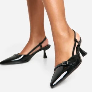 Svarta pumps med spetsig tå från Boohoo (slingbacks) - Snygga svarta pumps från Boohoo med en elegant spetsig tå och klack. Skorna har en glansig finish och en smal rem med spänne över foten för extra stil. Perfekta för att ge en chic touch till din outfit. Storlek 40 (wide fit) (Slingbacks/ kitten heel)